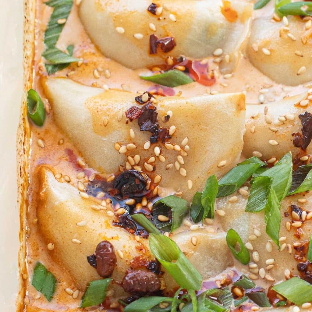close up of baked dumplings topped with sauce and chopped green onions