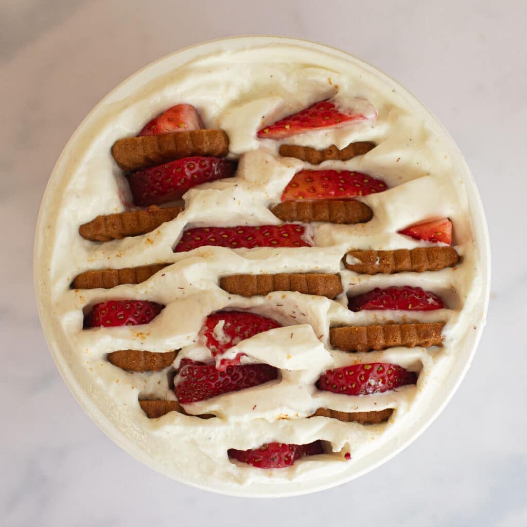 overhead view of a container of yogurt with Biscoff cookies and sliced strawberries inserted into it 