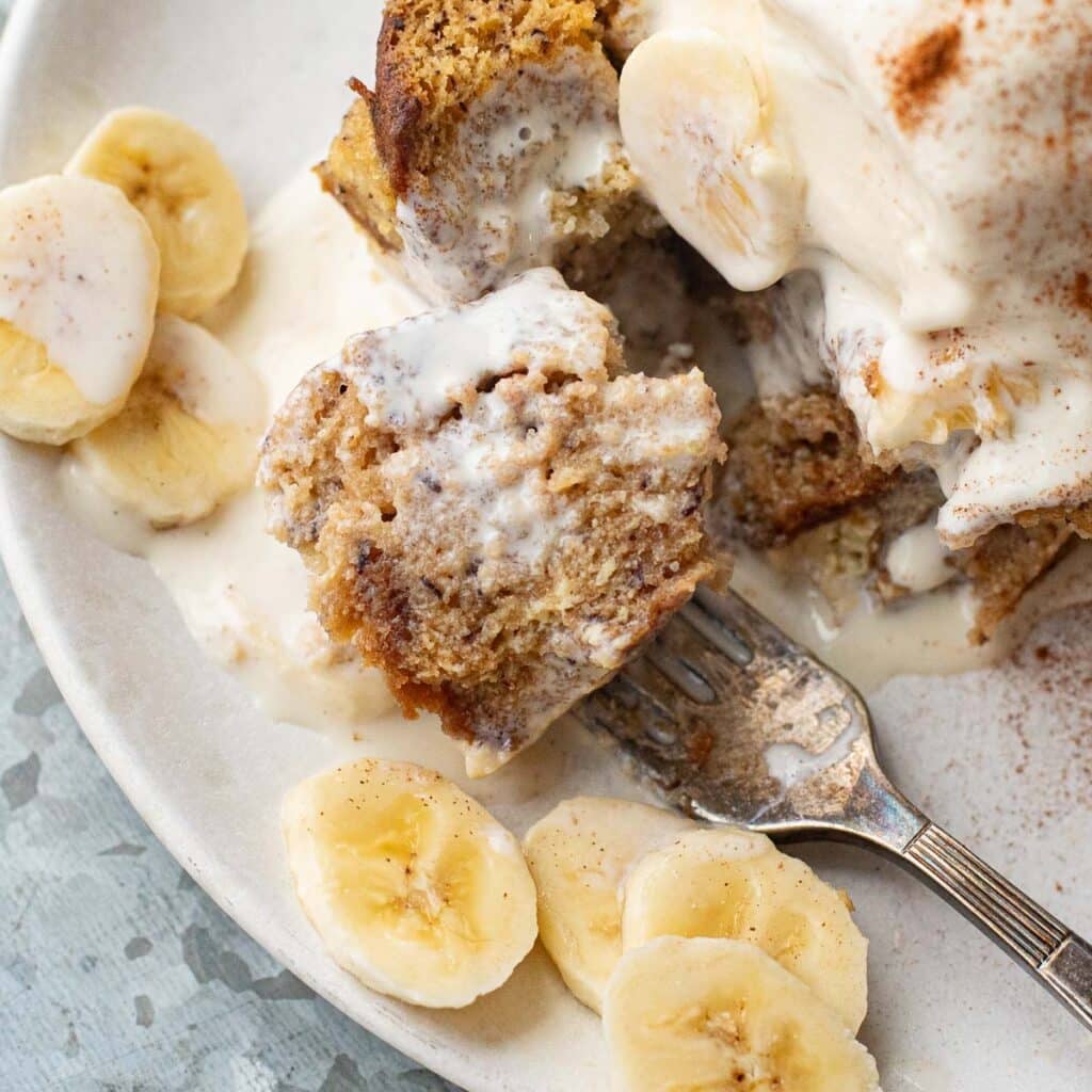 a fork holding a piece of banana bread bread pudding on a white plate