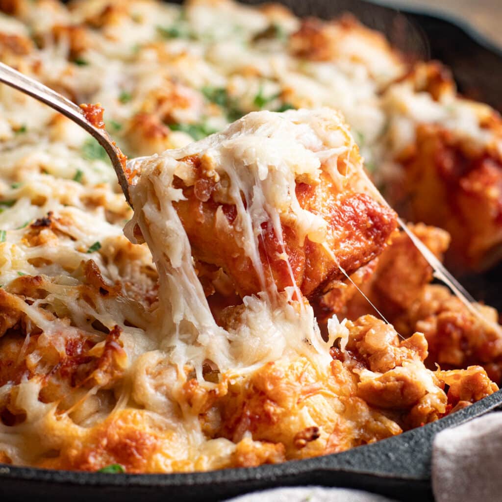 a spoon lifting a piece of bubble up pizza out of a cast iron pan