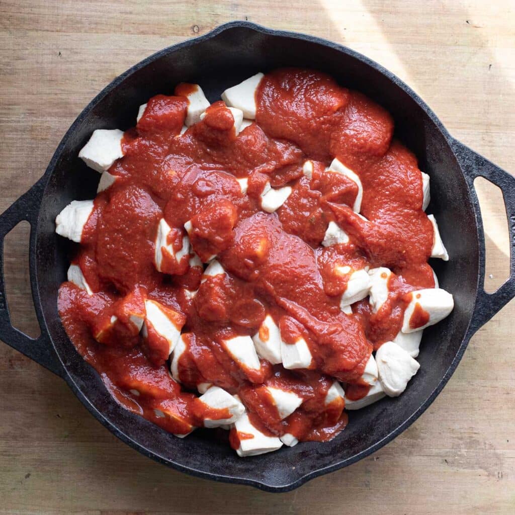quartered biscuit dough topped with pizza sauce in a cast iron pan