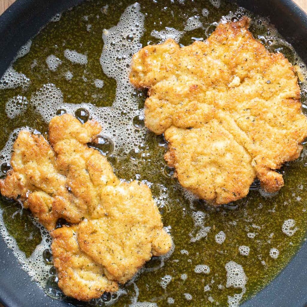 chicken cutlets frying in oil in a pan