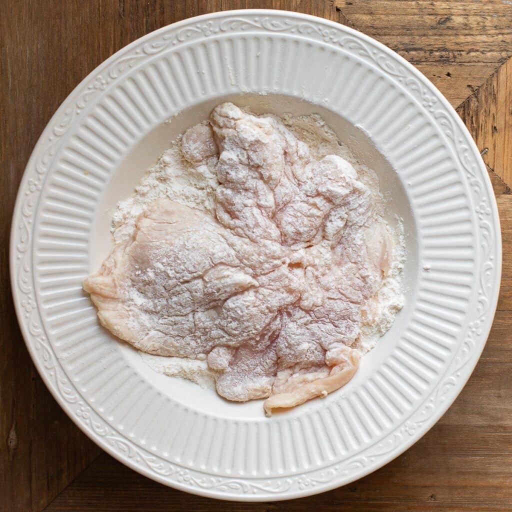 chicken breast being dredged in flour