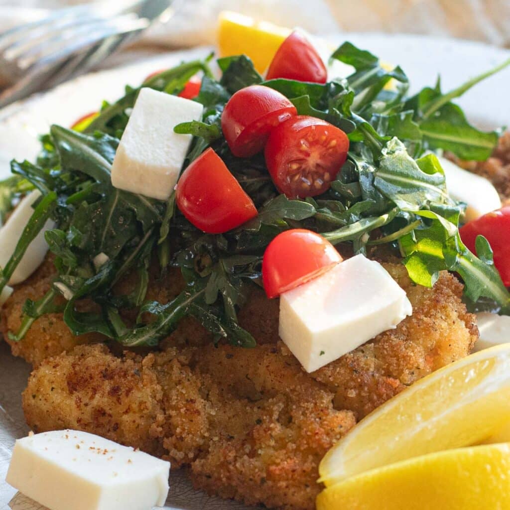 Chicken Milanese topped with arugula, tomatoes, mozzarella cheese and lemon wedges