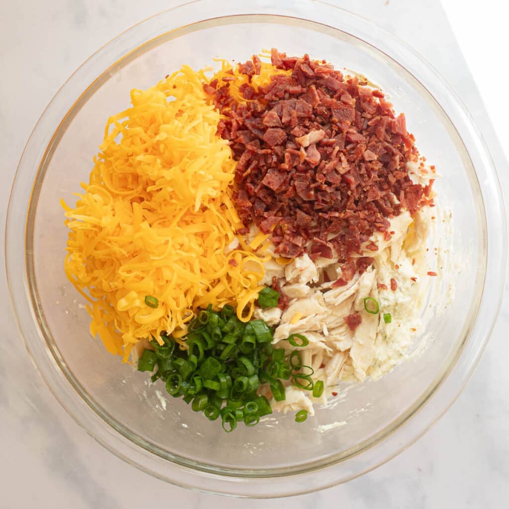 chopped bacon, grated cheddar cheese, chopped green onions and shredded chicken in a glass mixing bowl