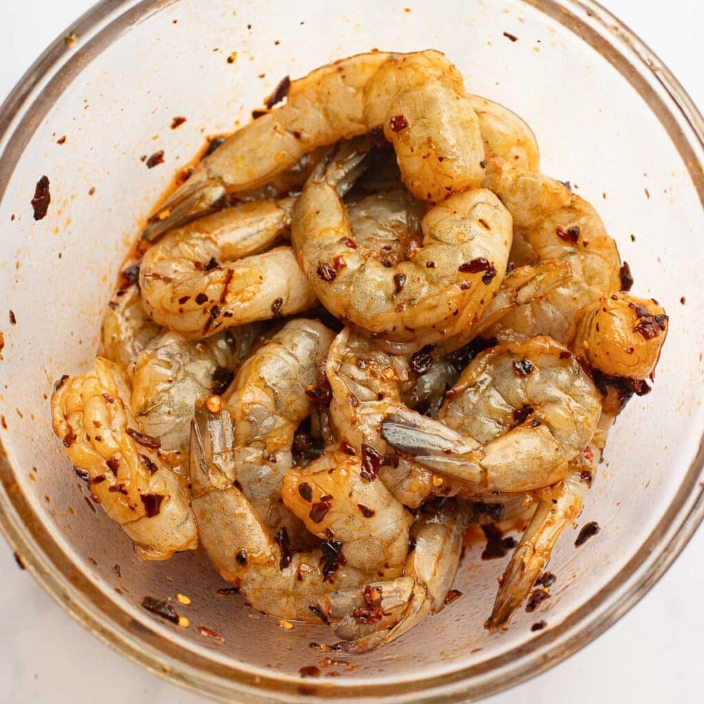 shrimp marinating in chili crisp in a glass bowl