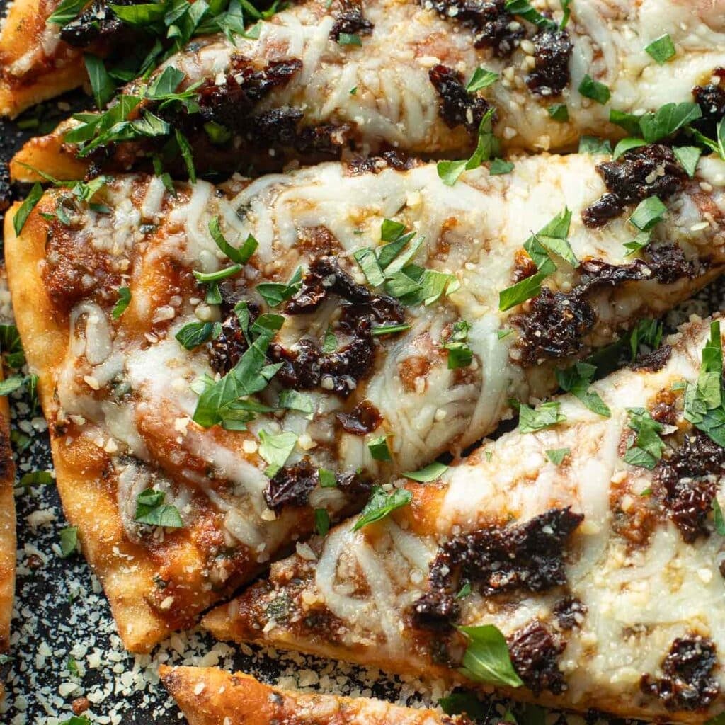naan pizza topped with cheese, sundried tomatoes and chopped fresh parsley