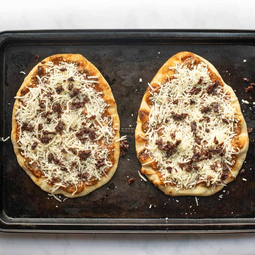 two naan pizzas on a baking sheet before being baked