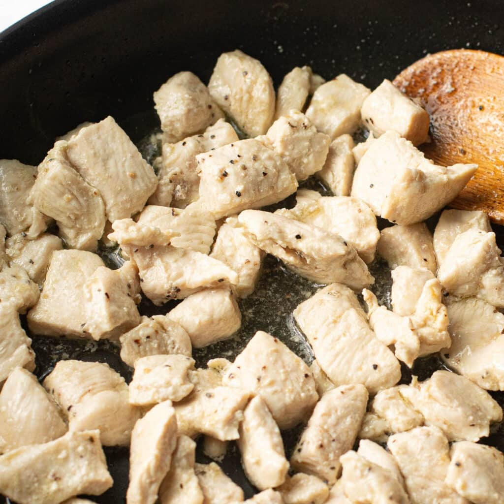 cubed pieces of chicken breast cooking in a pan