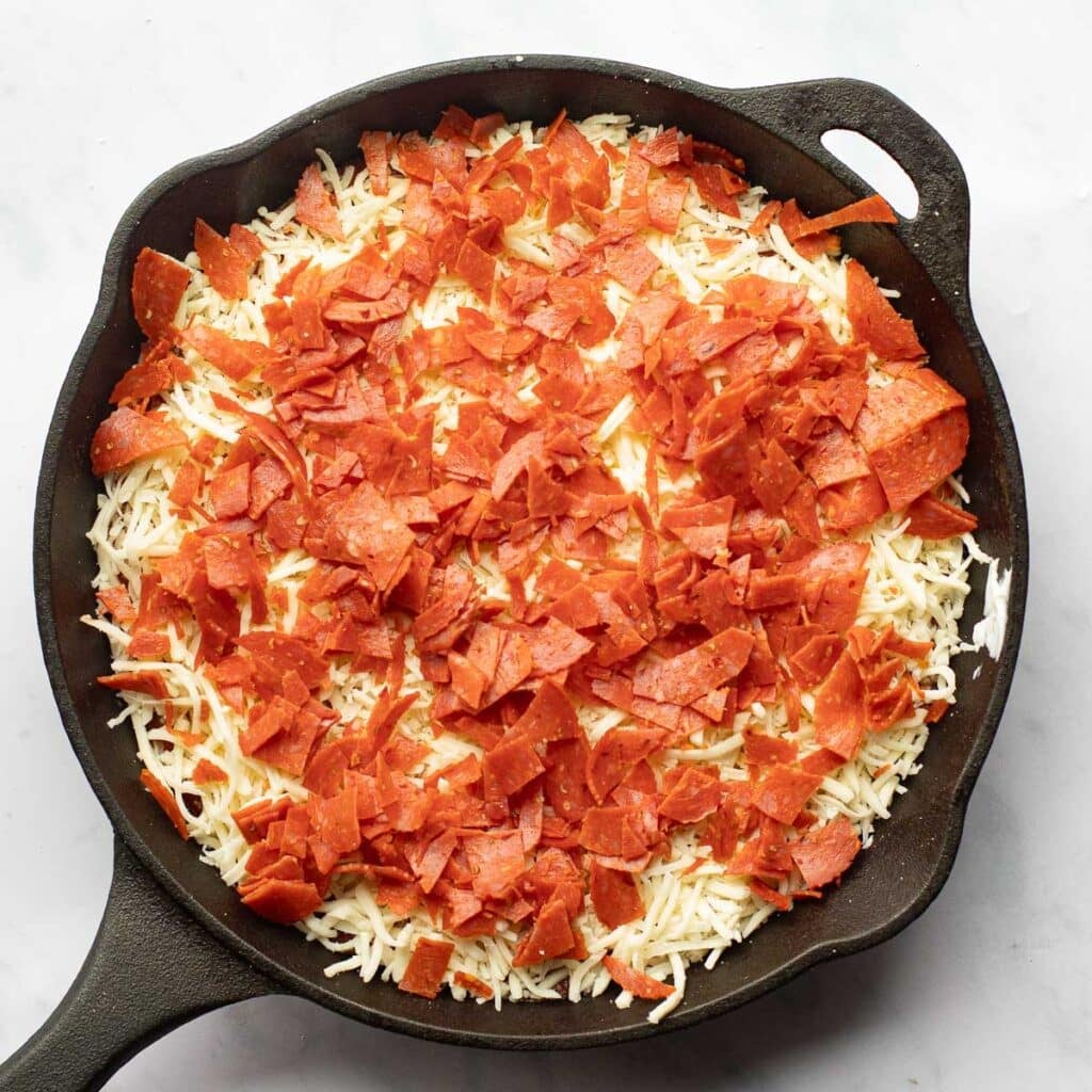 chopped pepperoni over shredded mozzarella cheese in a cast iron skillet