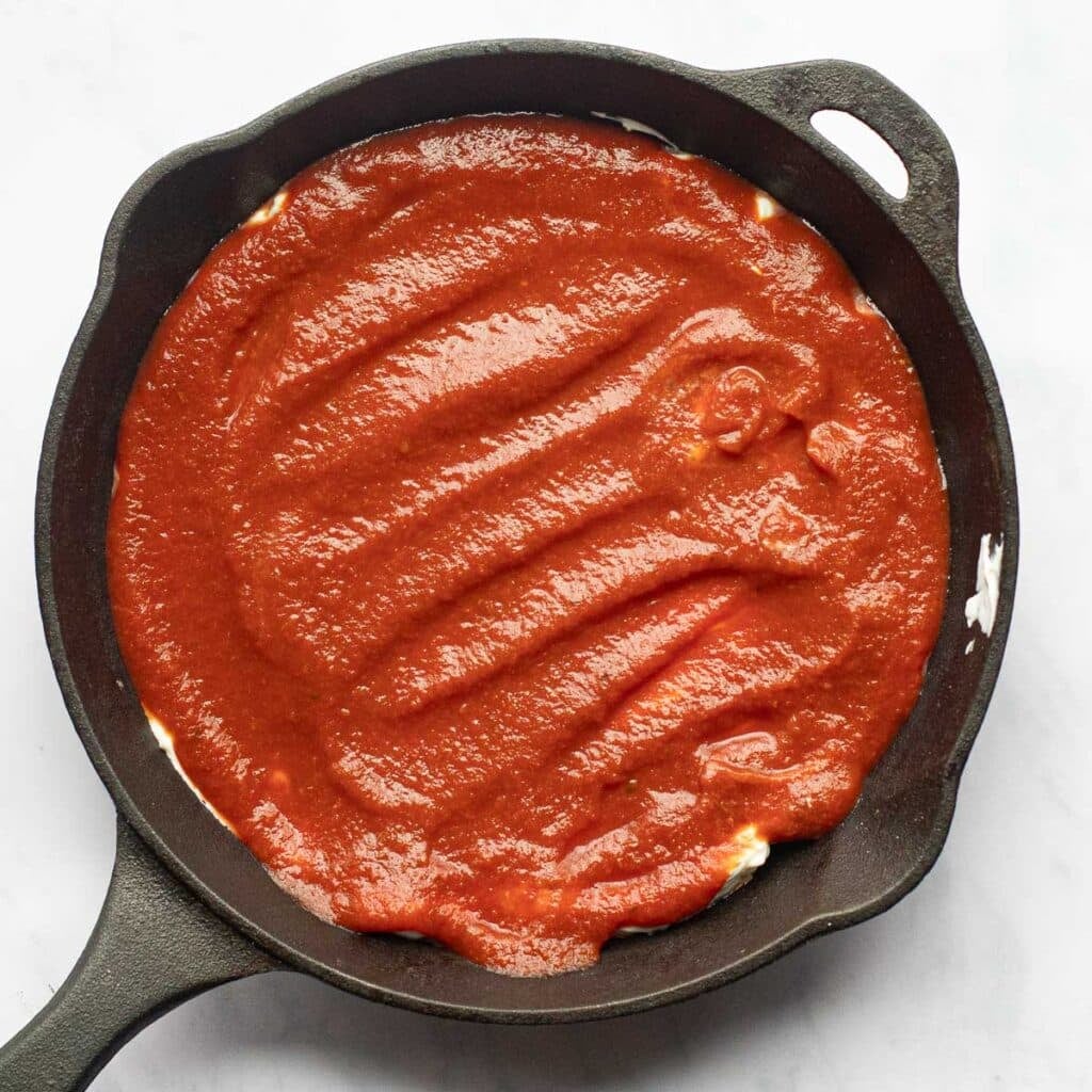 pizza sauce spread over cream cheese in a cast iron skillet