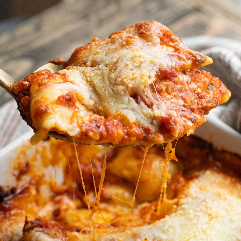 a serving spoon lifting baked ravioli out of the baking dish
