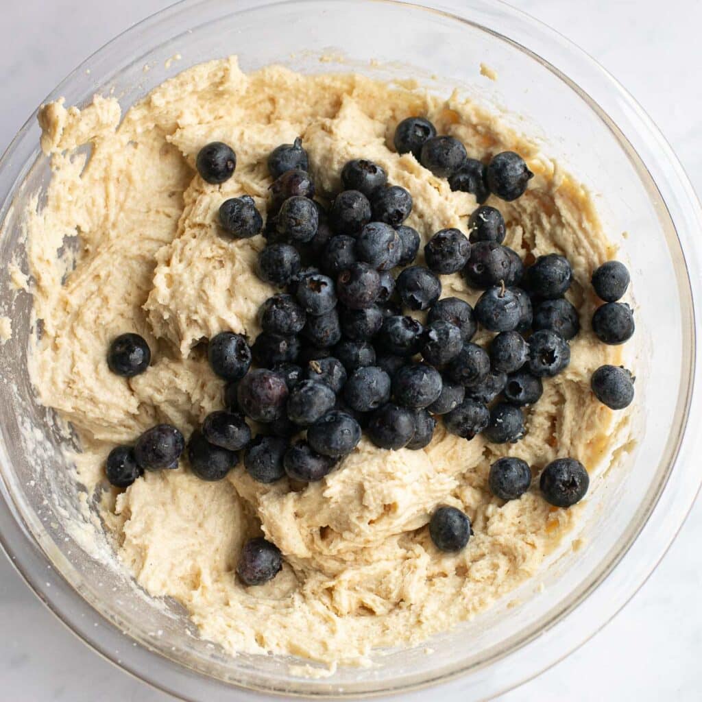 fresh blueberries on top of muffin batter in a glass mixing bowl