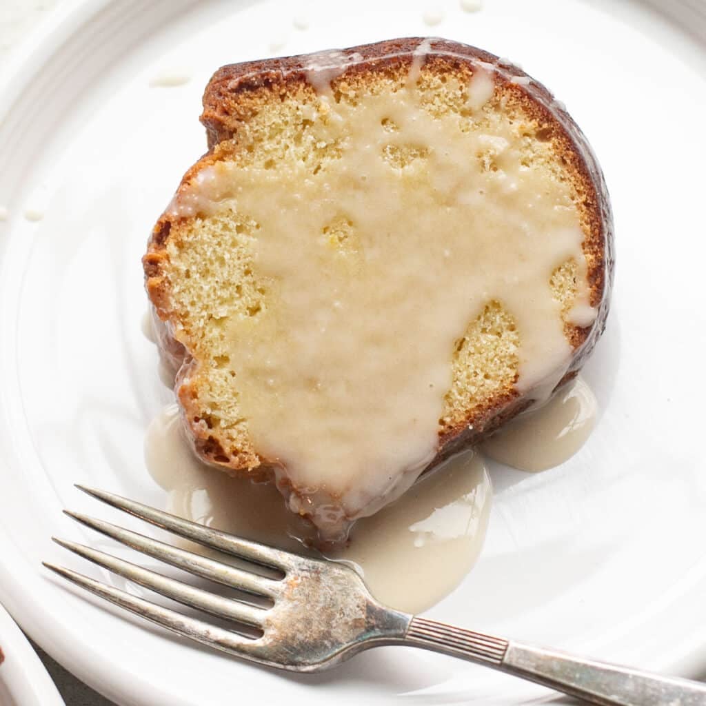 a slice of bourbon sour cream cake drizzled with maple glaze on a white plate with a silver fork