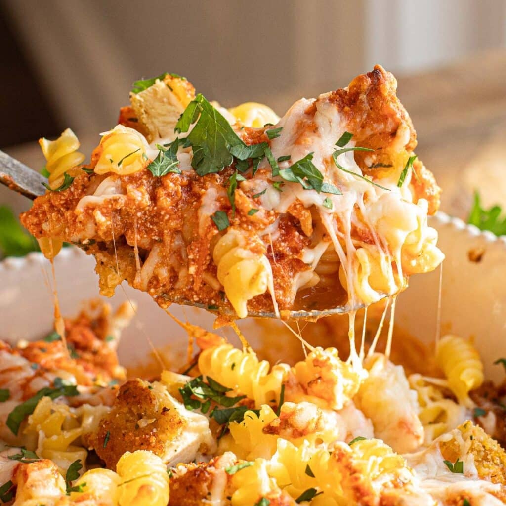 a serving spoon lifting chicken parm casserole out of the baking dish