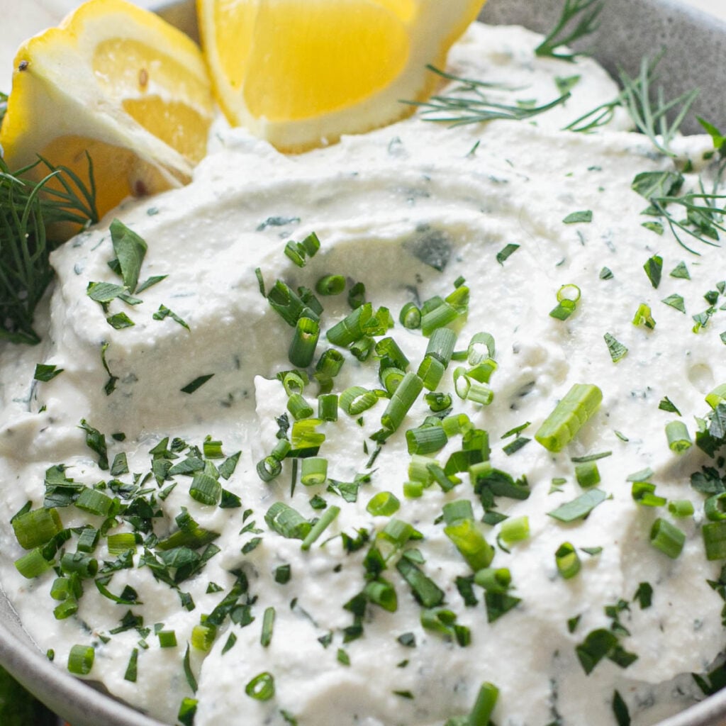 cottage cheese ranch dip in a gray bowl topped with fresh chives and lemon wedges