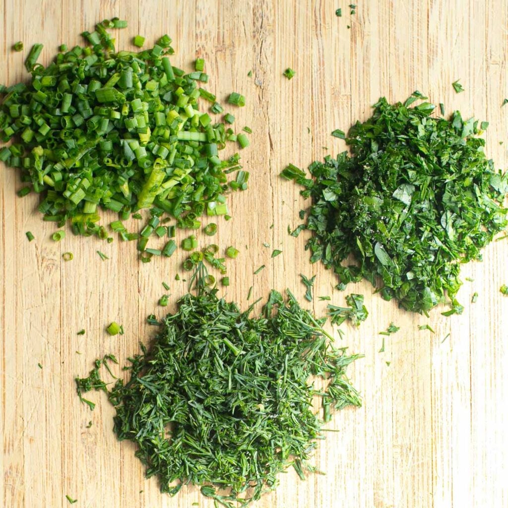 finely chopped chives, parsley and dill on a wooden cutting board