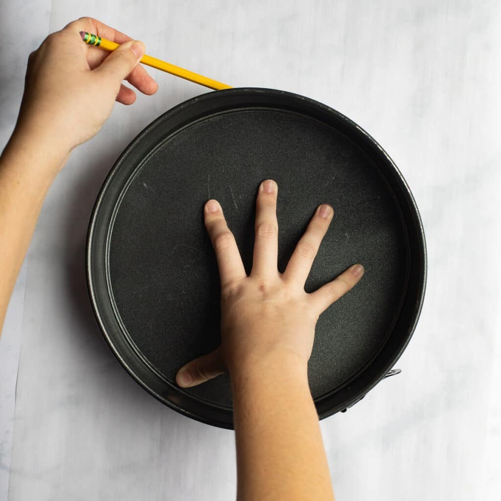 a hand tracing a parchment paper circle around a springform pan