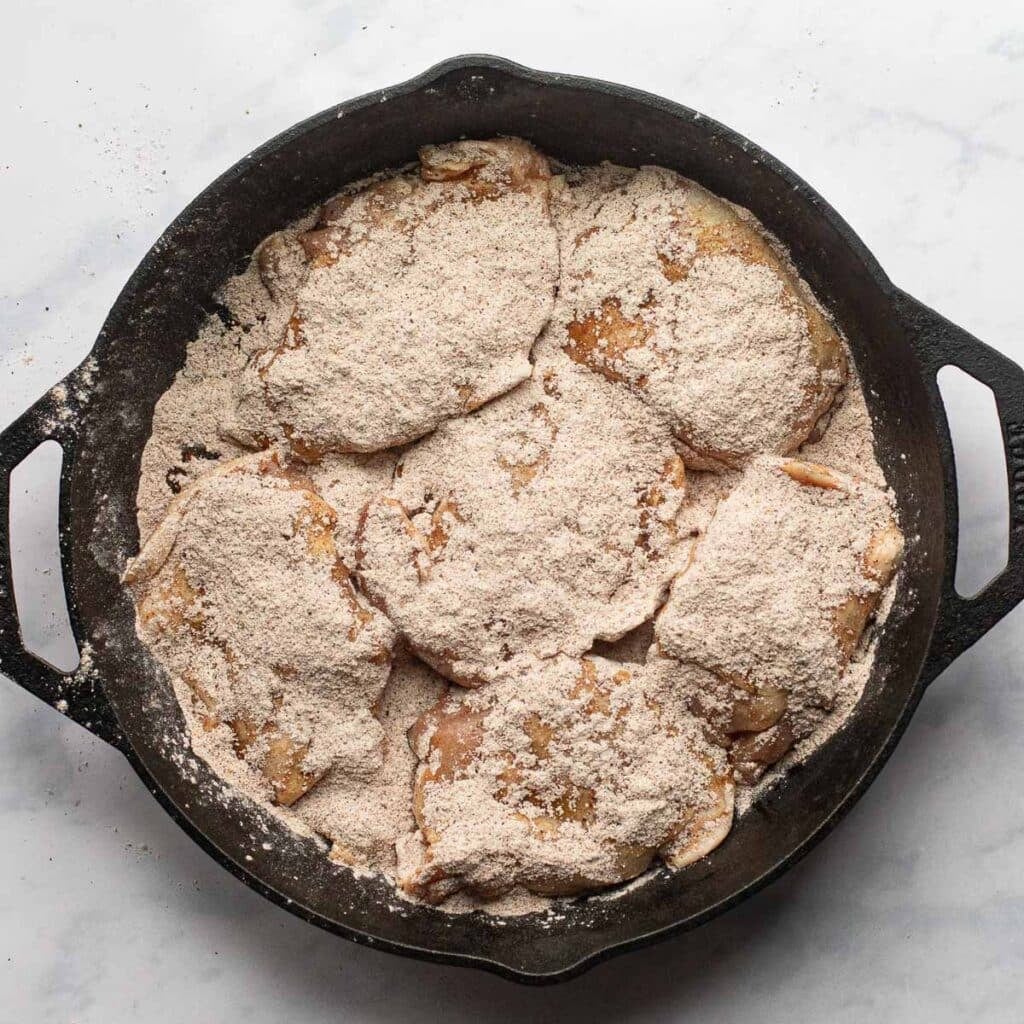 chicken thighs topped with dry seasonings in a cast iron pan