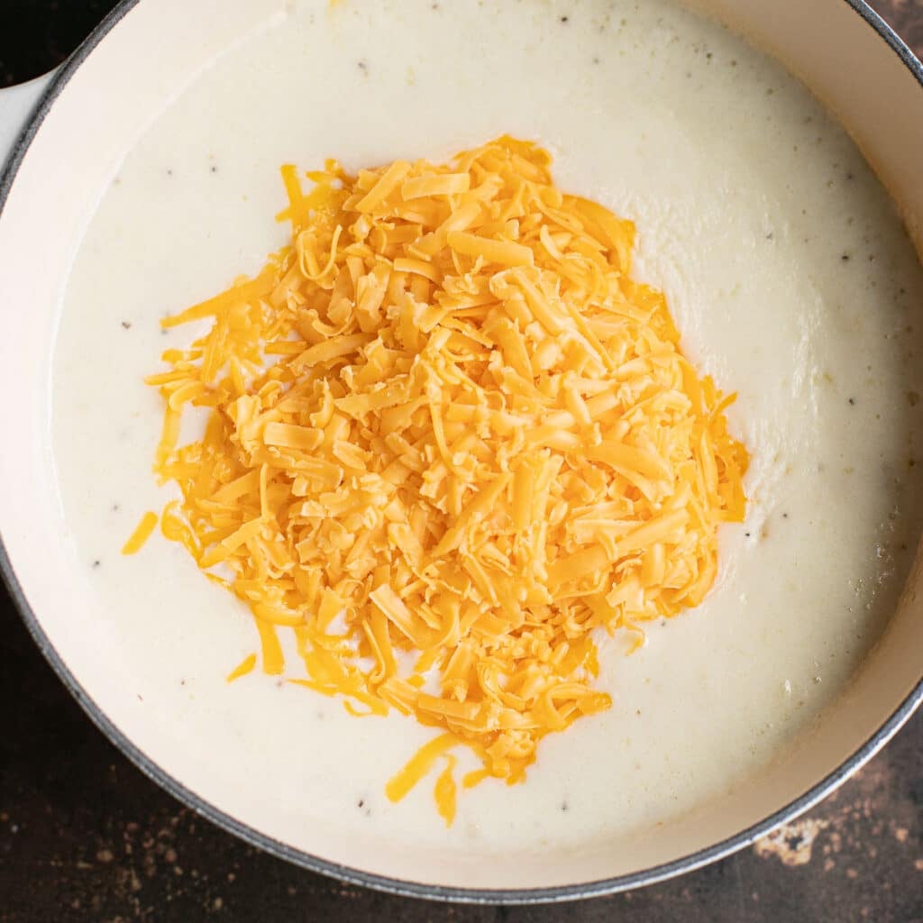 shredded cheddar cheese in a pile on top of bechamel sauce in a saucepan