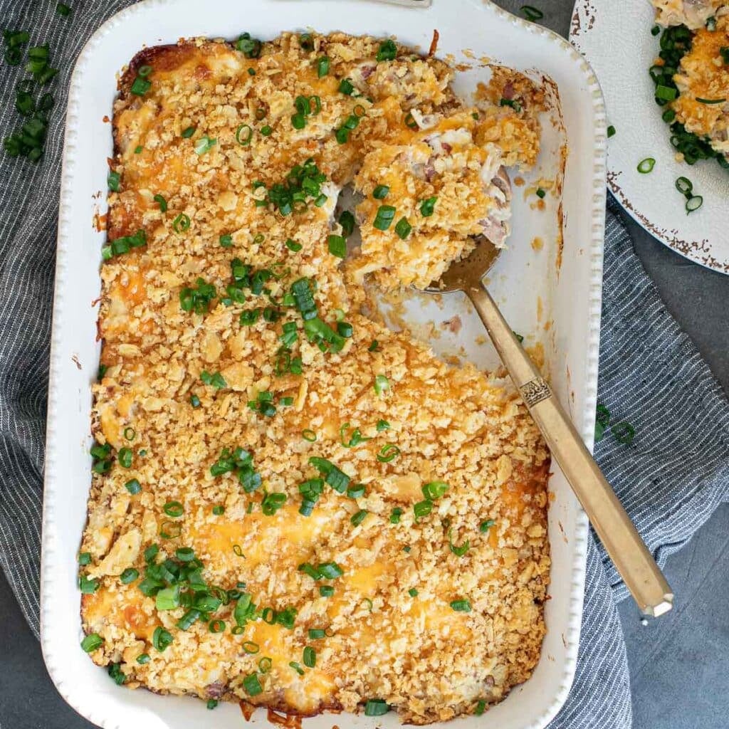 million dollar chicken casserole in a white casserole dish with a gold serving spoon