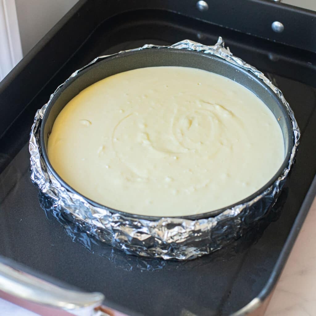 unbaked cheesecake in a springform pan inside a water bath