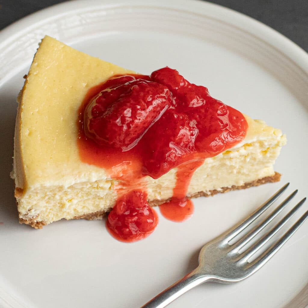 a slice of New York Cheesecake topped with strawberry sauce
