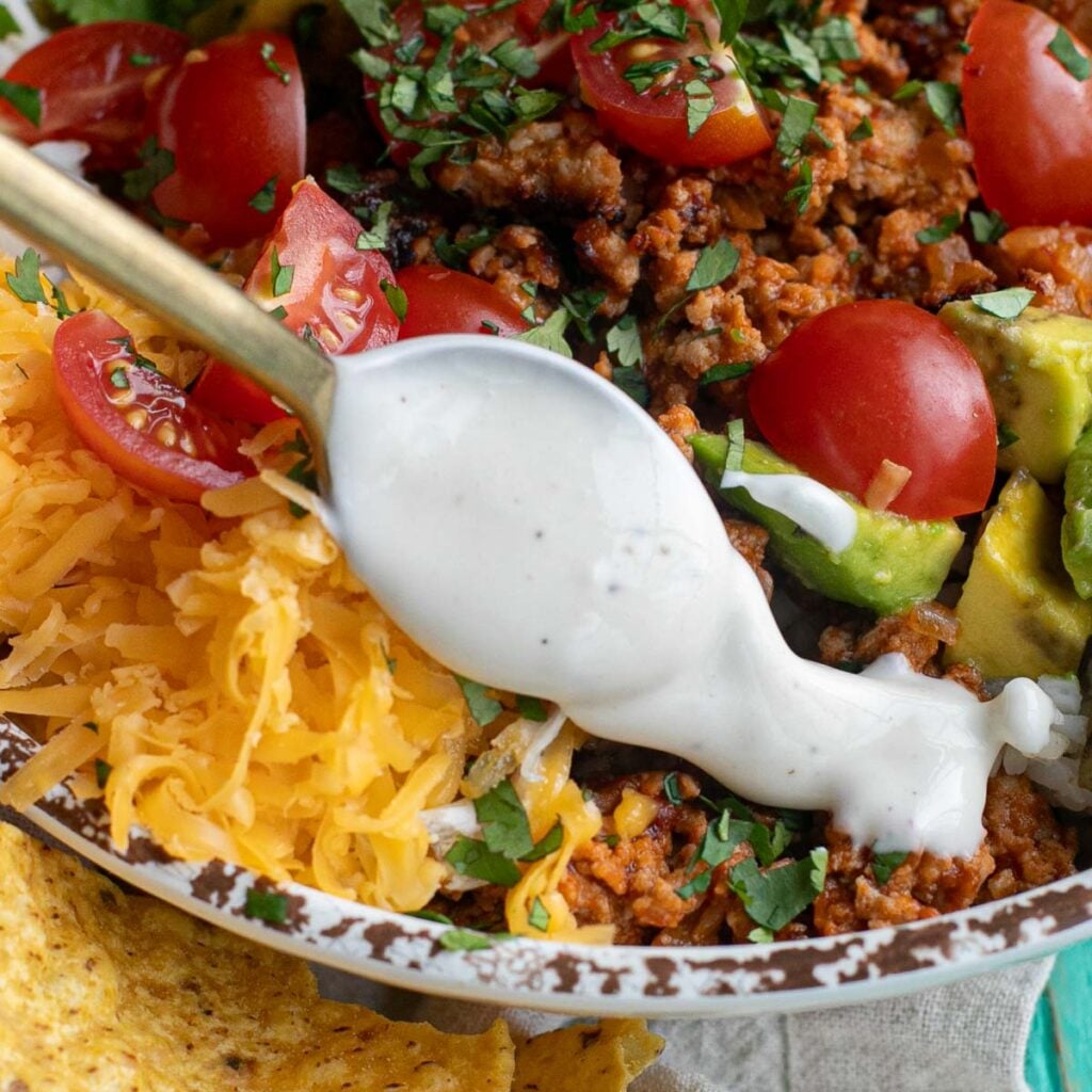 a spoon drizzling ranch dressing on a taco salad