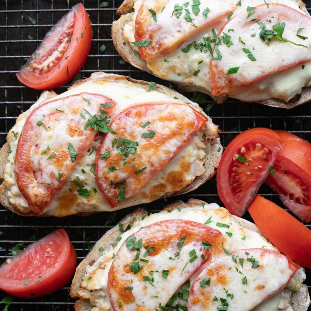 open faced tuna melt sandwich on a wire rack with tomato wedges