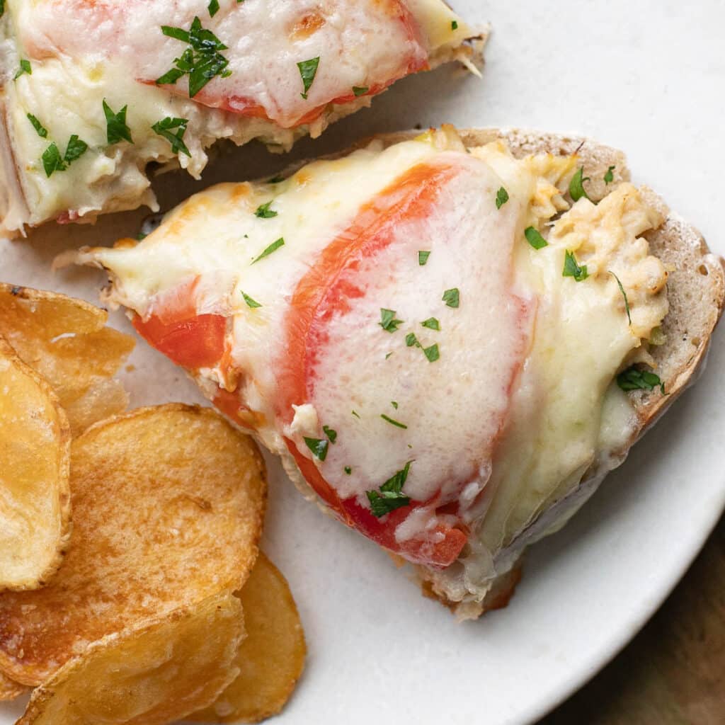 Tuna Melt sandwich cut in half with a side of potato chips on a white plate