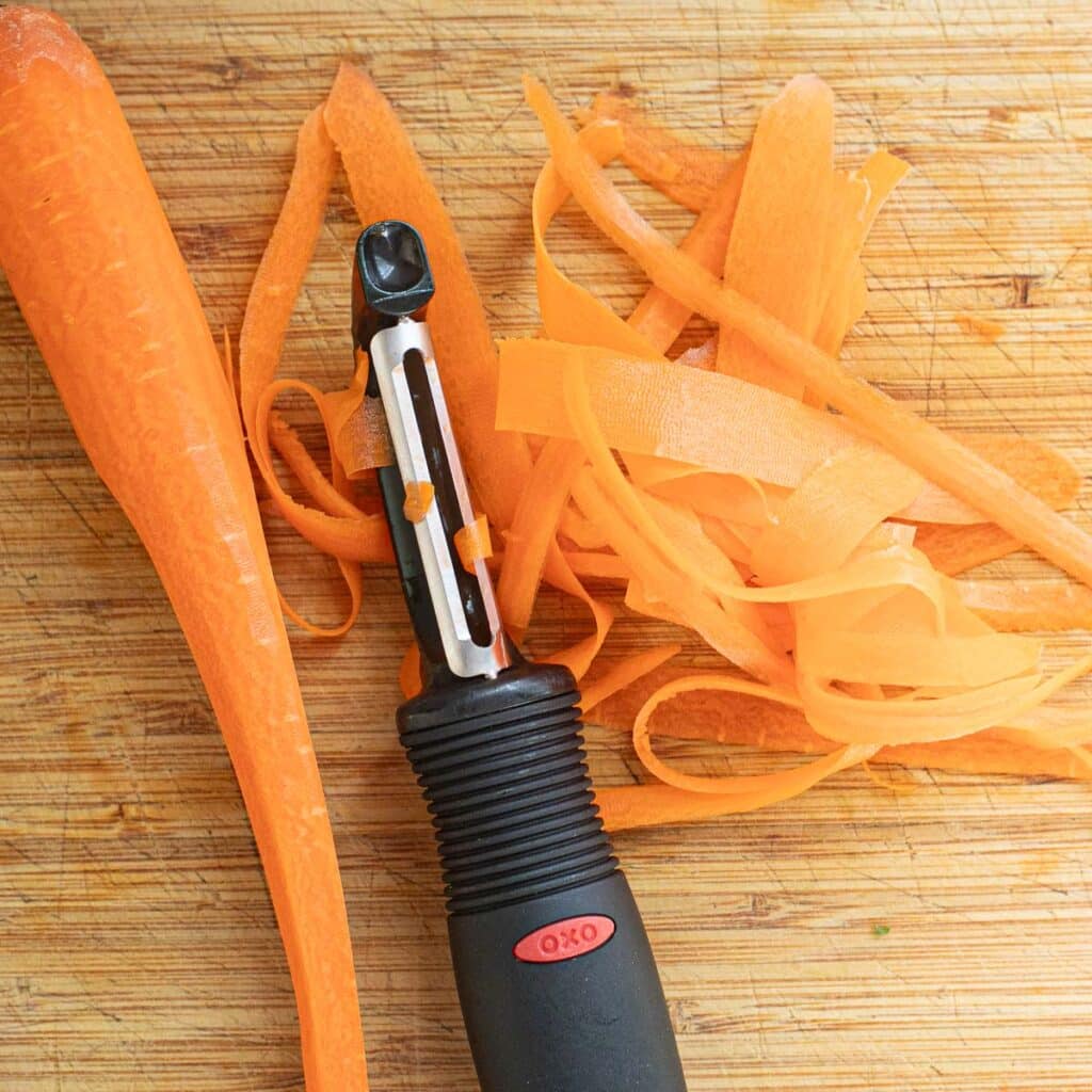 carrot ribbons and a vegetable peeler on a wooden cutting board