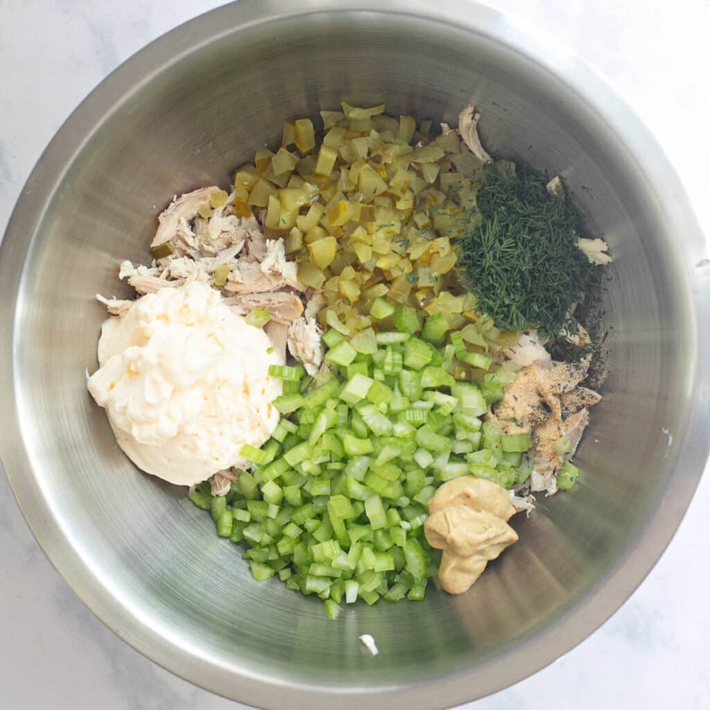 mayonnaise, diced celery, diced pickles, chopped dill and shredded chicken in a mixing bowl