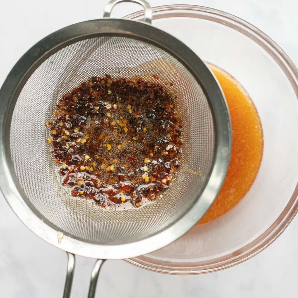 red pepper flakes being strained out of hot honey