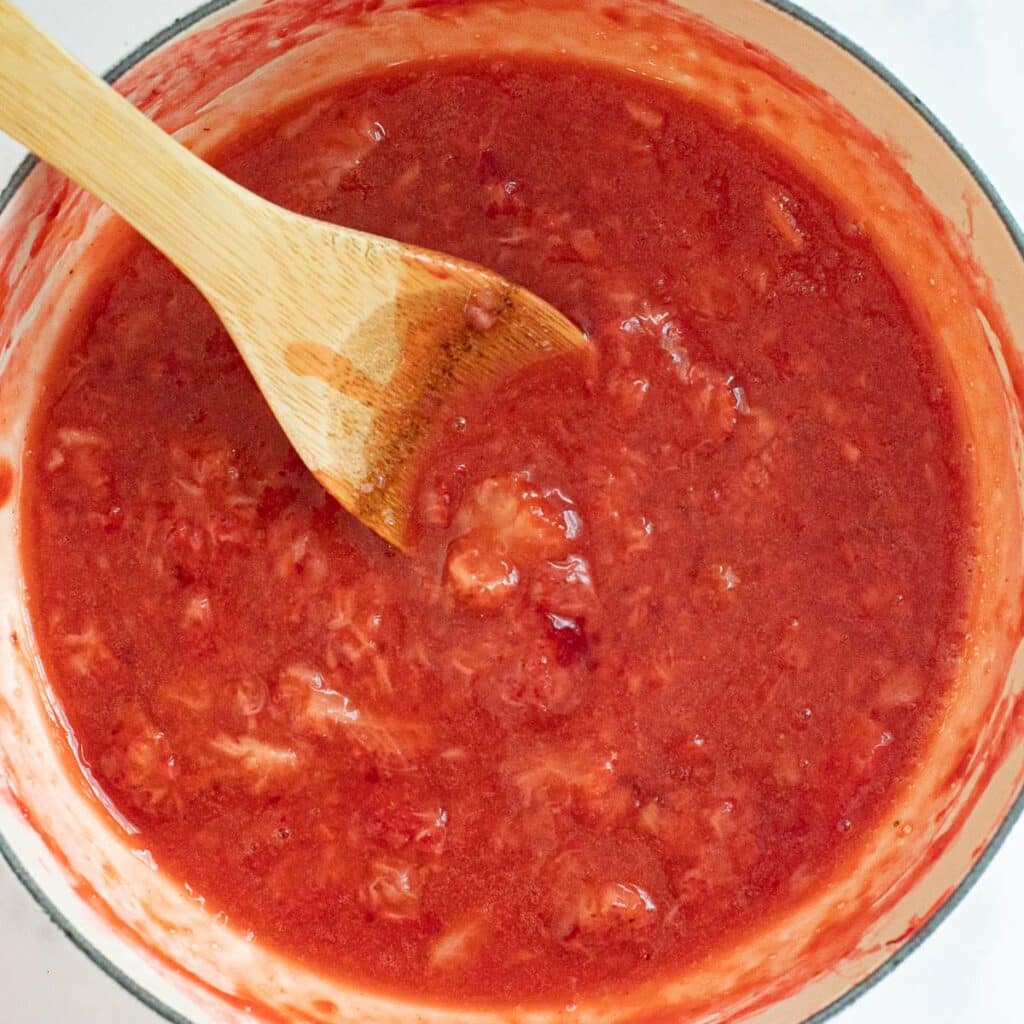 strawberry sauce in a white saucepan with a wooden spoon