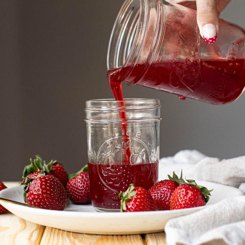 strawberry syrup being poured from one mason jar into a smaller mason jar