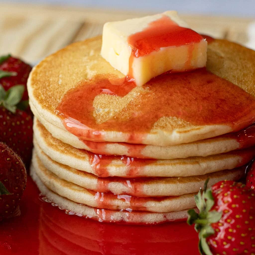 strawberry syrup dripping down the sides of a stack of pancakes
