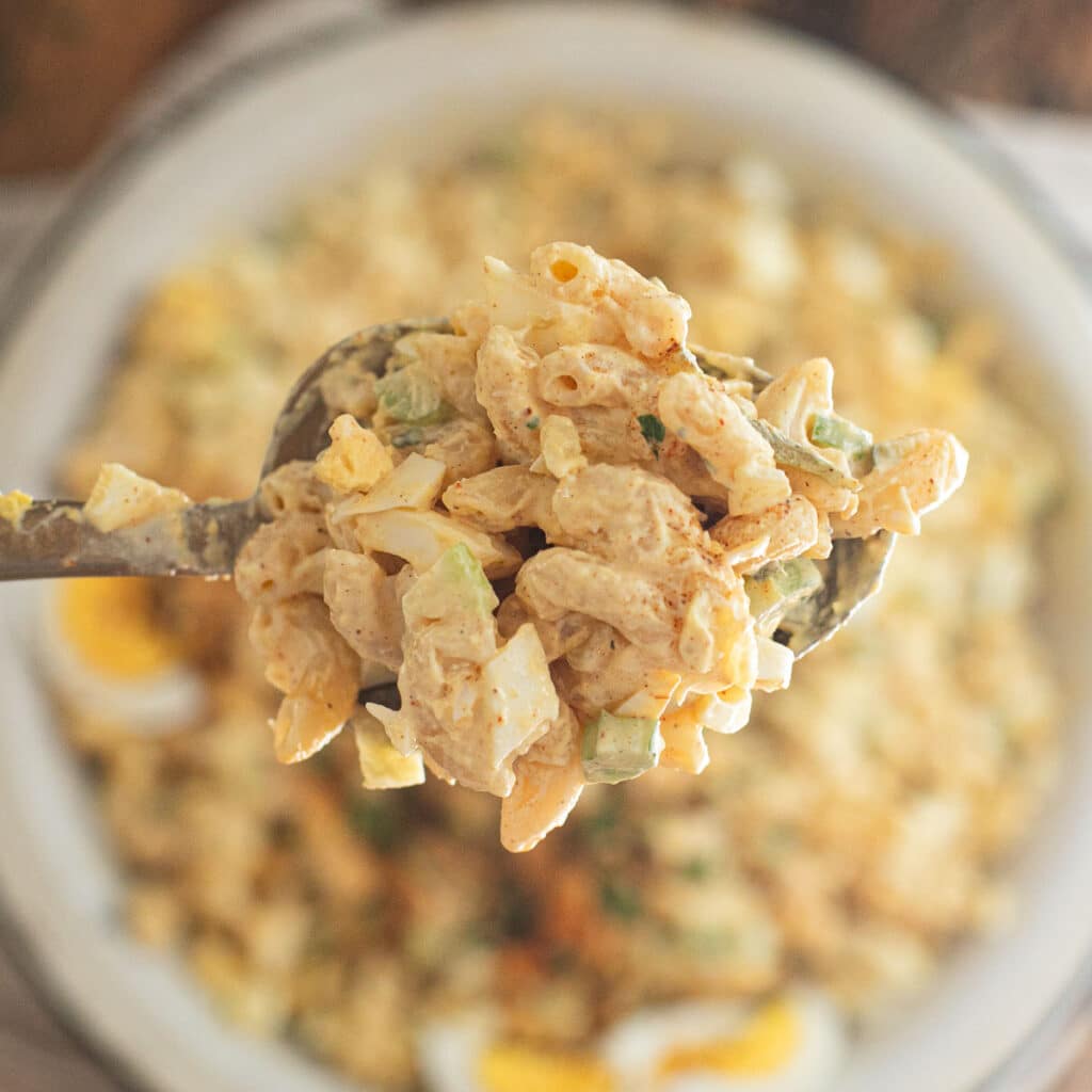 a large spoon holding deviled egg macaroni salad 