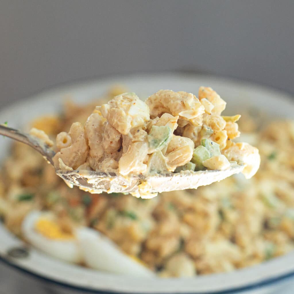 a large spoon holding deviled egg macaroni salad 