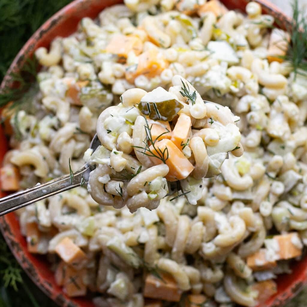 a large spoon holding dill pickle macaroni salad