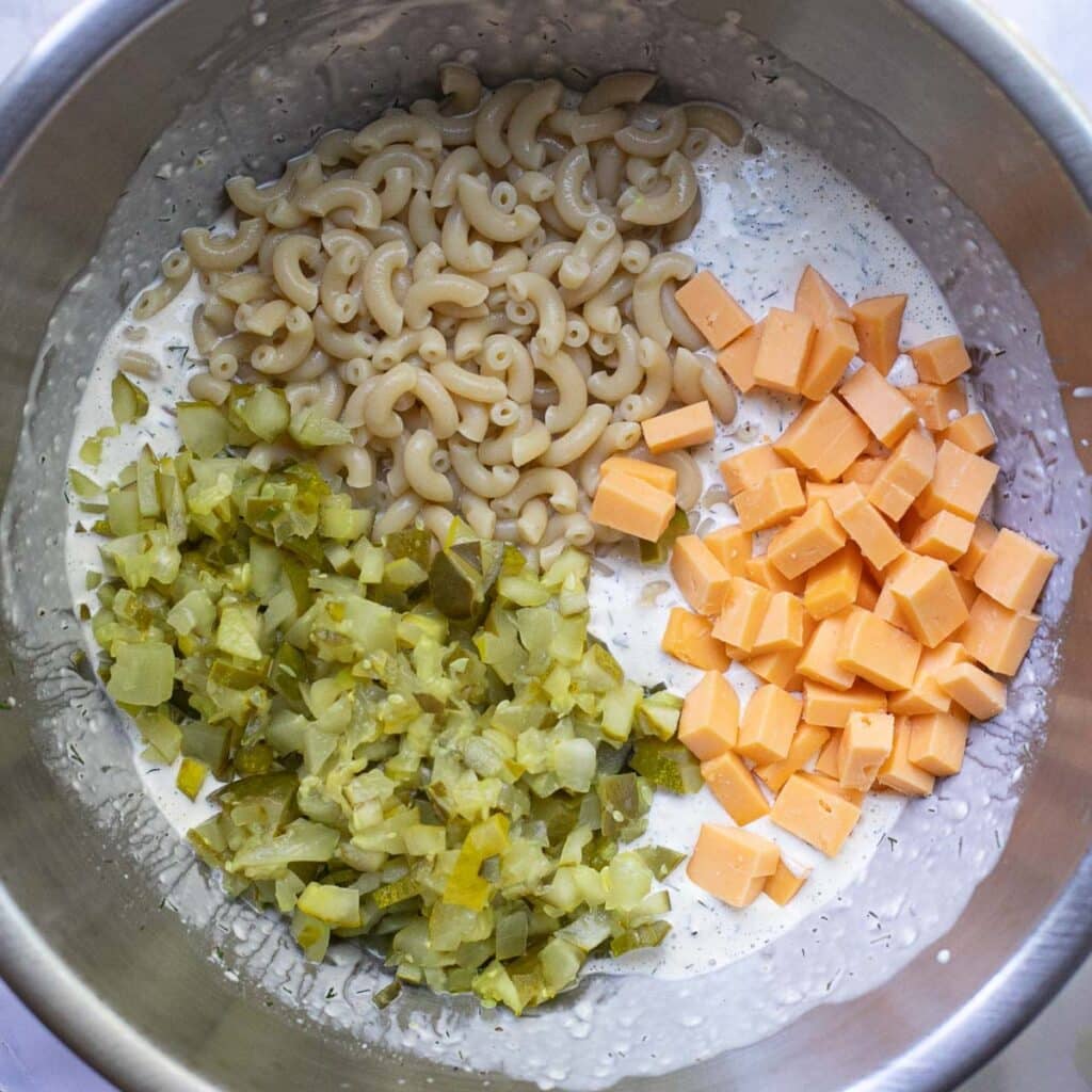 cubed cheddar cheese, elbow macaroni and chopped pickles in a silver mixing bowl