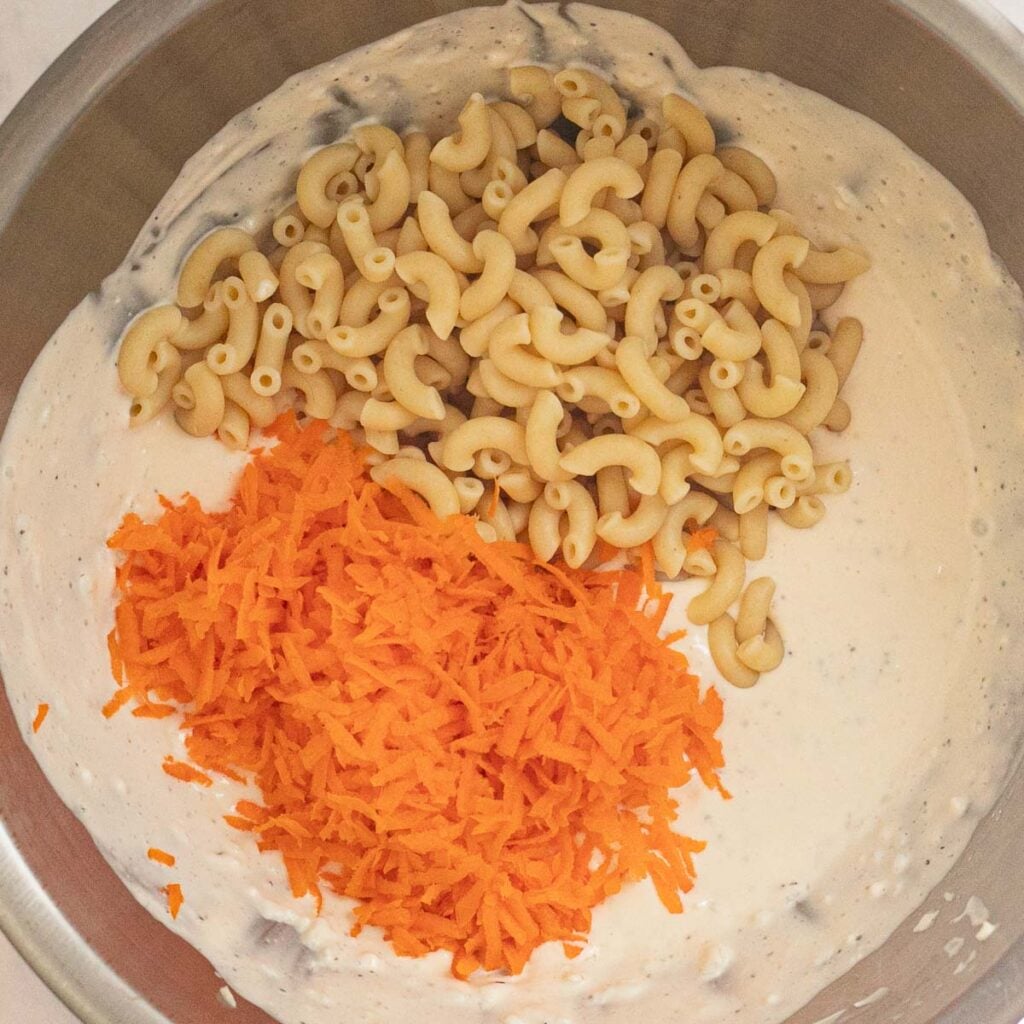elbow macaroni and grated carrot with mayonnaise dressing in a mixing bowl