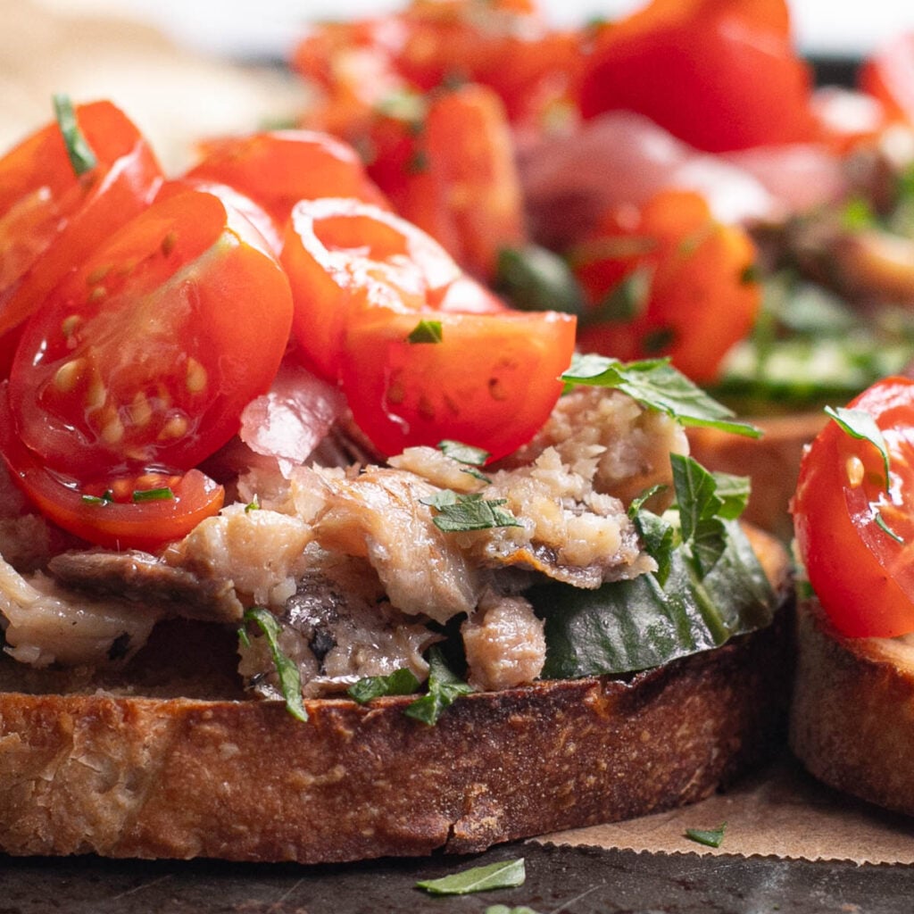 sideways view of a piece of sardine toast with chopped tomatoes and fresh parsley