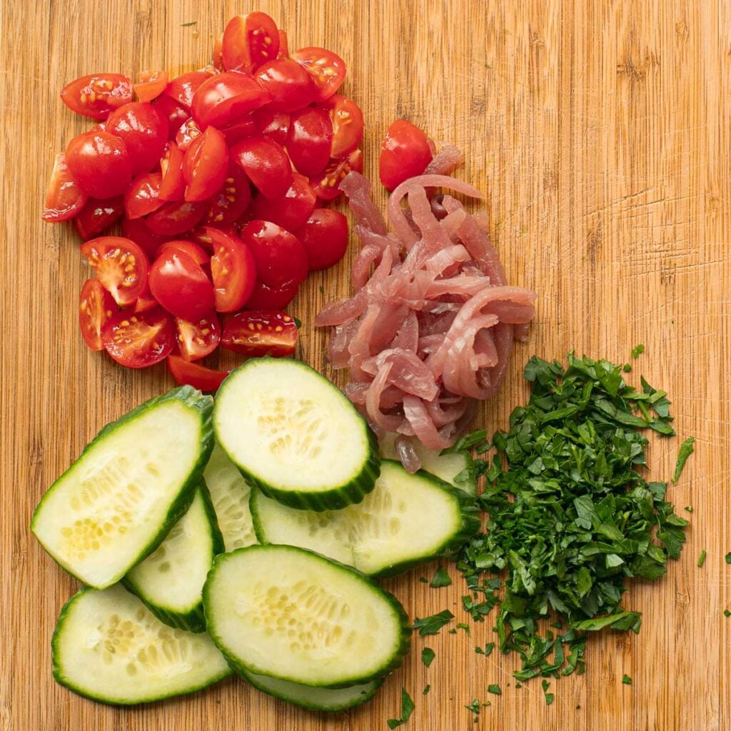 chopped tomatoes, pickled onions, sliced cucumbers and chopped parsley on a wooden board