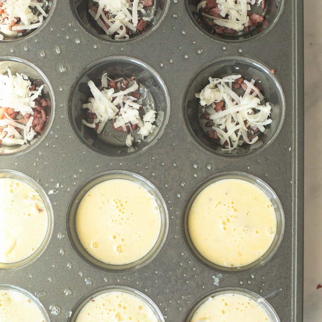 a muffin pan filled with grated cheese and diced bacon