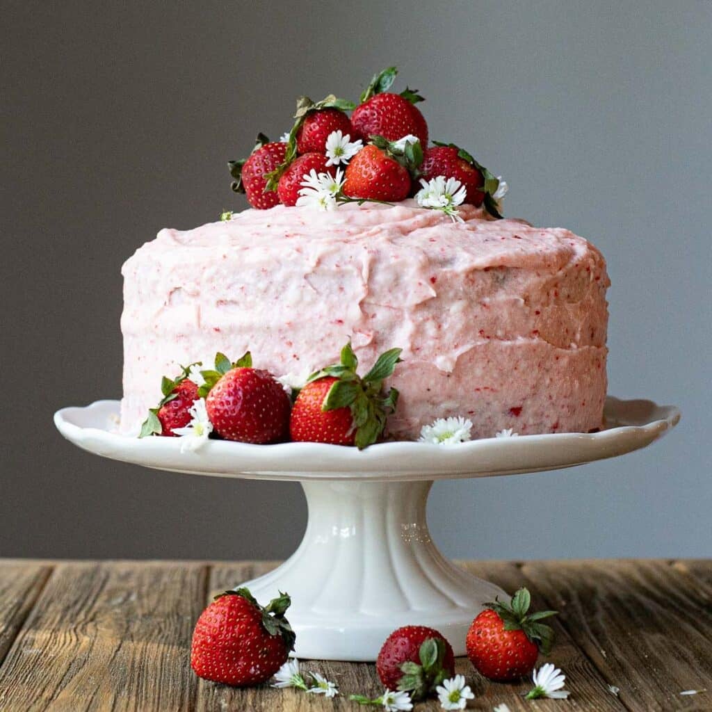 strawberry cake on a white cake stand topped with fresh strawberries