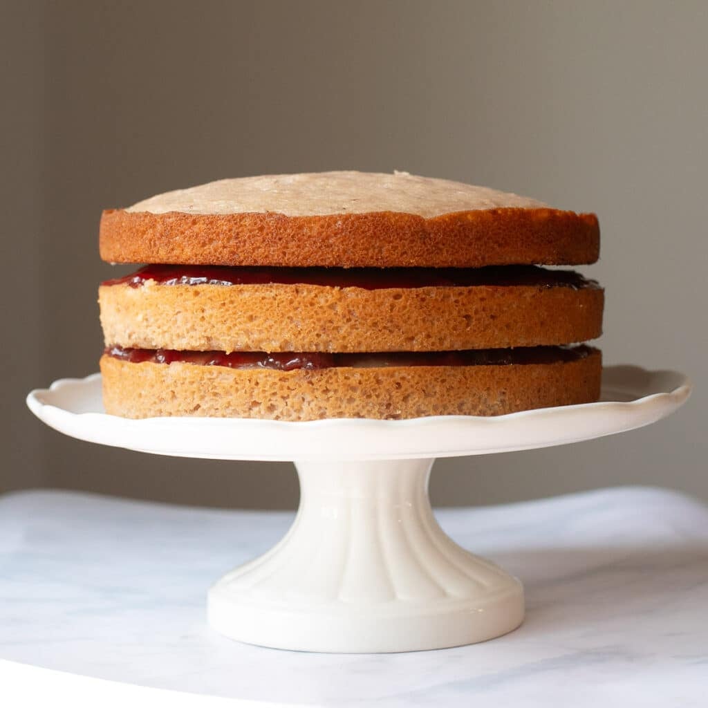 three layers of strawberry cake with jam in between them on a white cake stand