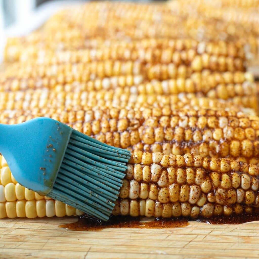 seasonings being brushed onto an ear of corn