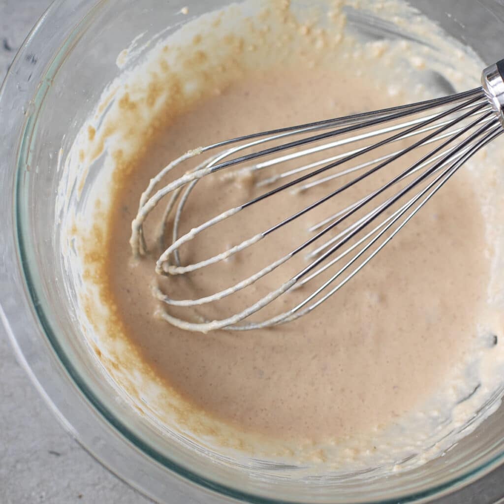 Caesar dressing in a glass bowl with a wire whisk