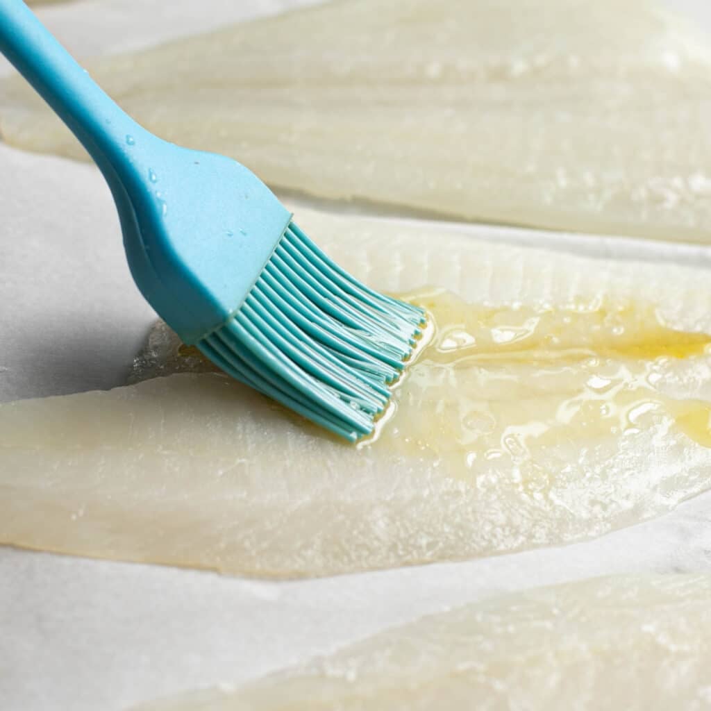 oil being applied to a flounder fillet with a pastry brush