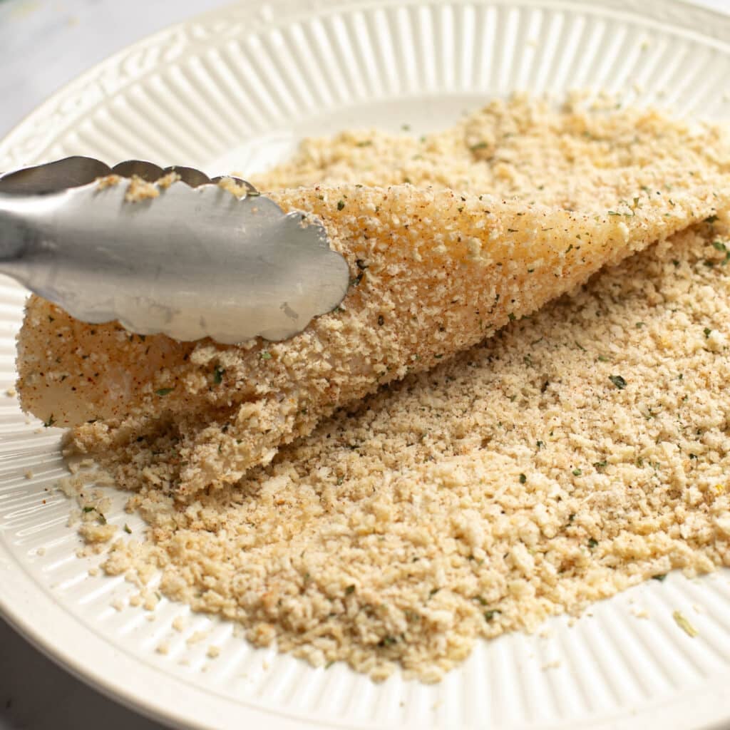 a flounder fillet being coated in Parmesan panko mixture